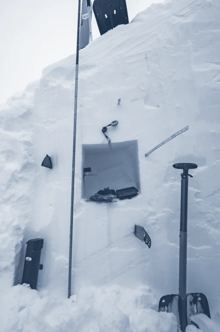 A snow pit wall with a probe and shovel, set up for a transceiver and snowpack lesson